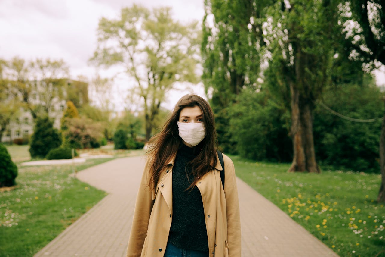 Woman wearing a face mask standing in a park surrounded by trees, illustrating outdoor protection.