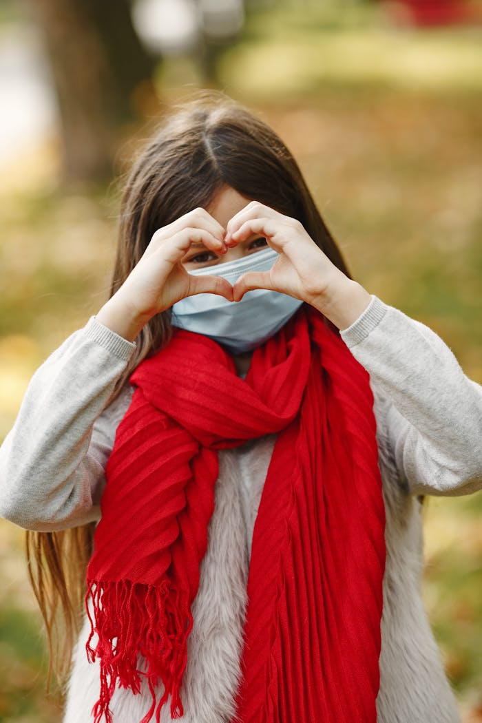 about-us-02 Girl in a mask and red scarf making a heart gesture during fall.